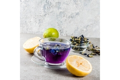 Glass cup of vibrant purple butterfly pea tea with lemons and dried flowers